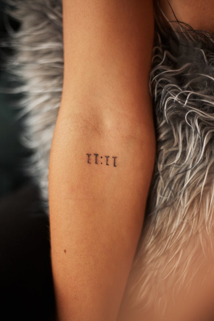 A close-up view of a minimalist tattoo reading '11:11' on an arm with a fur background.